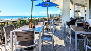 Un patio al aire libre con mesas y sillas, sombrillas azules y vista a la playa.