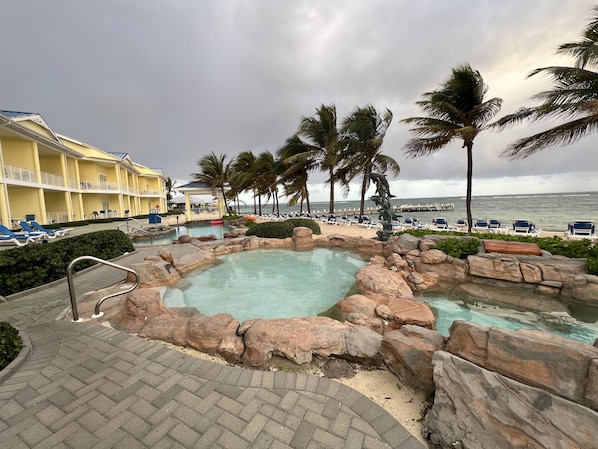 A resort pool area with a hot tub, lounge chairs, and a view of the ocean.
