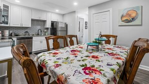 Een moderne keuken met witte kasten, een roestvrijstalen koelkast en een eettafel met een tafelkleed met bloemen.