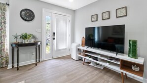 Een moderne woonkamer met een flatscreen televisie, een console tafel met decoratieve objecten, en een deur met zonwering.