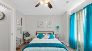Een slaapkamer met een bed, een plafondventilator, een klok en een raam met gordijnen.