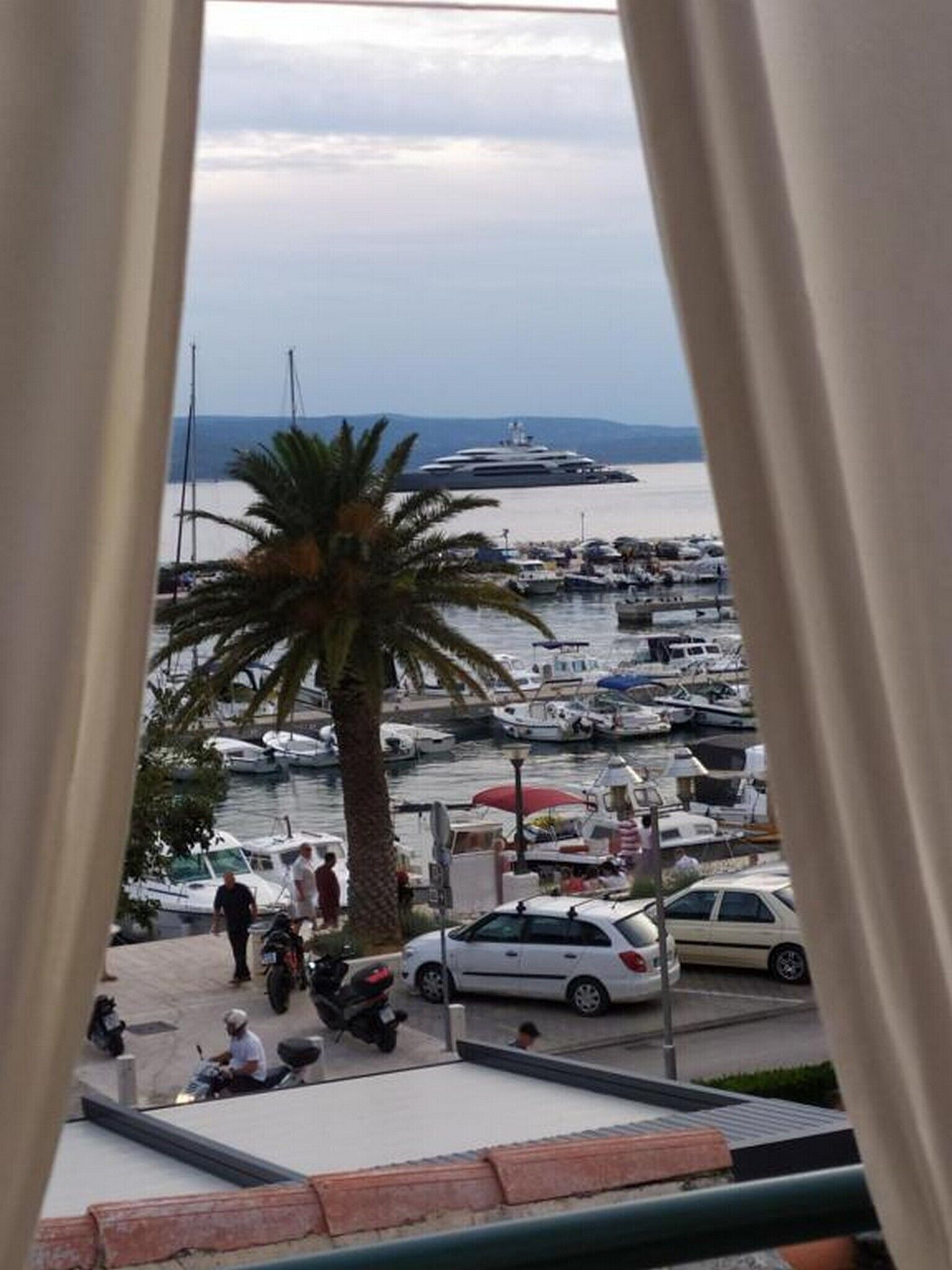 A marina with boats, a large yacht, and people walking.