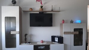 A modern living room with a flat-screen TV mounted on the wall, a coffee table with decorative items, and a cabinet with a glass door. - Apartment Kupre - One Bedroom Apartment with Sauna (Slavonski Brod)