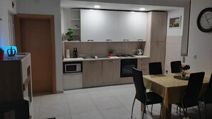A modern kitchen with white cabinets, a dining table with chairs, and a clock on the wall. - Apartment Kupre - One Bedroom Apartment with Sauna (Slavonski Brod)