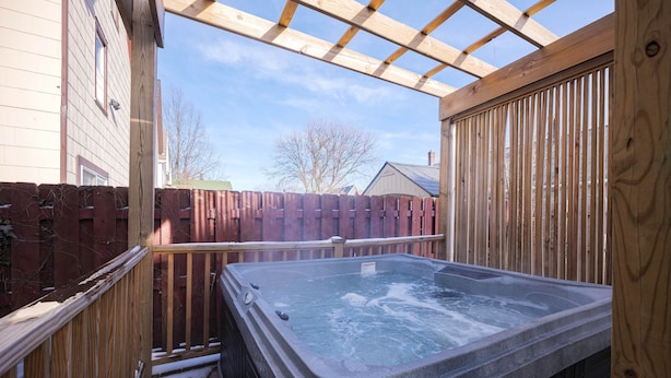 A hot tub in a wooden deck area with a wooden fence and a pergola overhead.