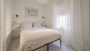 A minimalist bedroom with a bed, bedside lamps, a framed artwork, and sheer curtains.