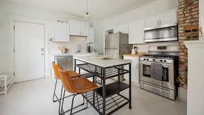 A modern kitchen with white cabinets, stainless steel appliances, and a brick accent wall.