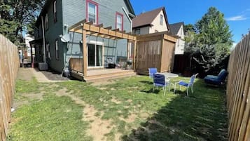 Ein Garten mit einer Holzterrasse, einer überdachten Veranda und einem Rasen.