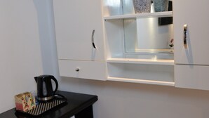 Angolo cottura con macchina del caffè, piccolo frigorifero e pianta in vaso su uno scaffale.