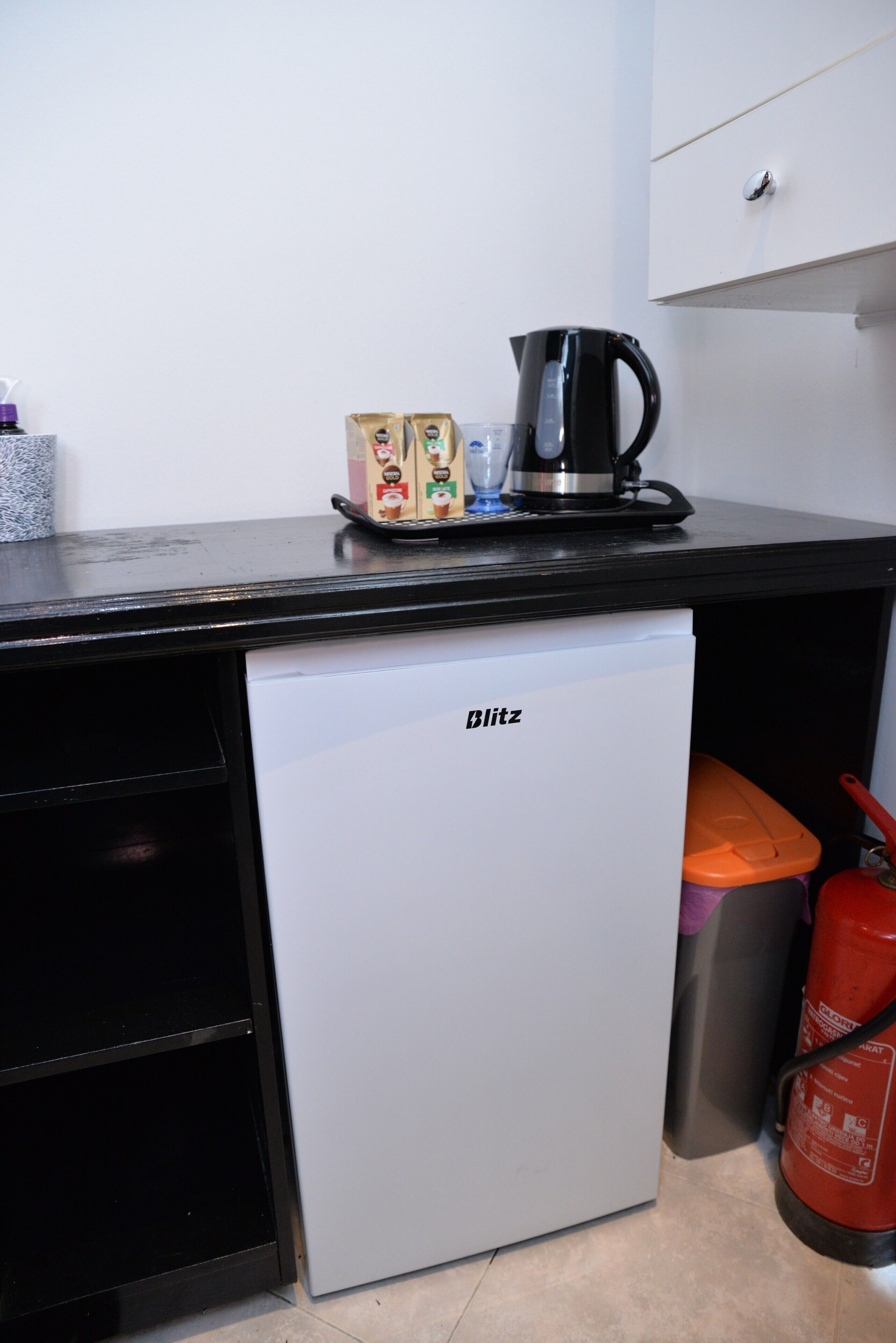 A compact kitchenette with a refrigerator, a coffee maker, and a fire extinguisher.