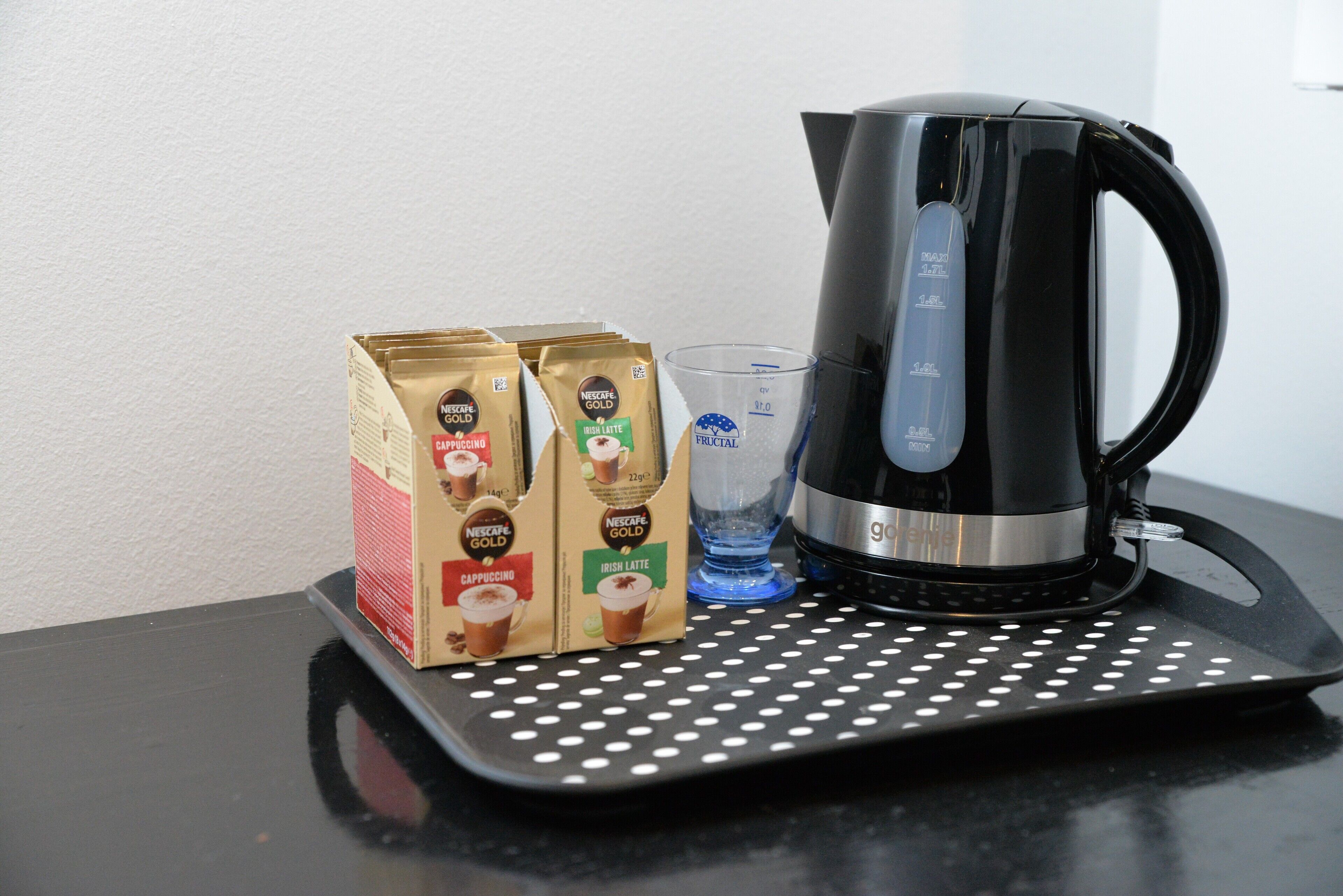A coffee maker, two boxes of Nescafe Gold coffee pods, and a glass on a black tray with white polka dots.