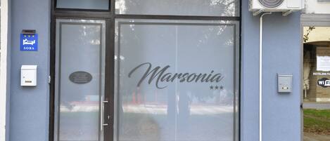 A storefront with a frosted glass door, a sign reading "Marsonia," and a Beko inverter unit mounted on the wall.