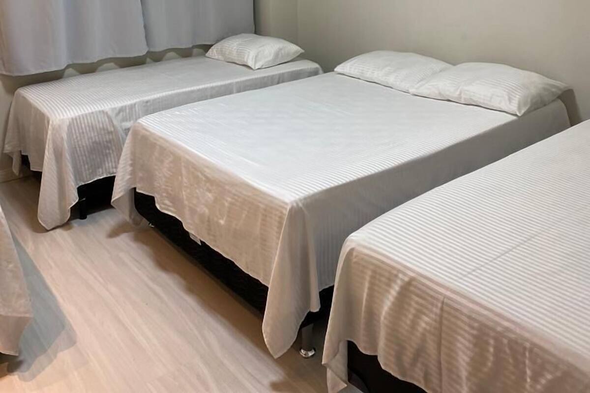 Quarto com três camas de solteiro, ventoinha no teto e ar condicionado.