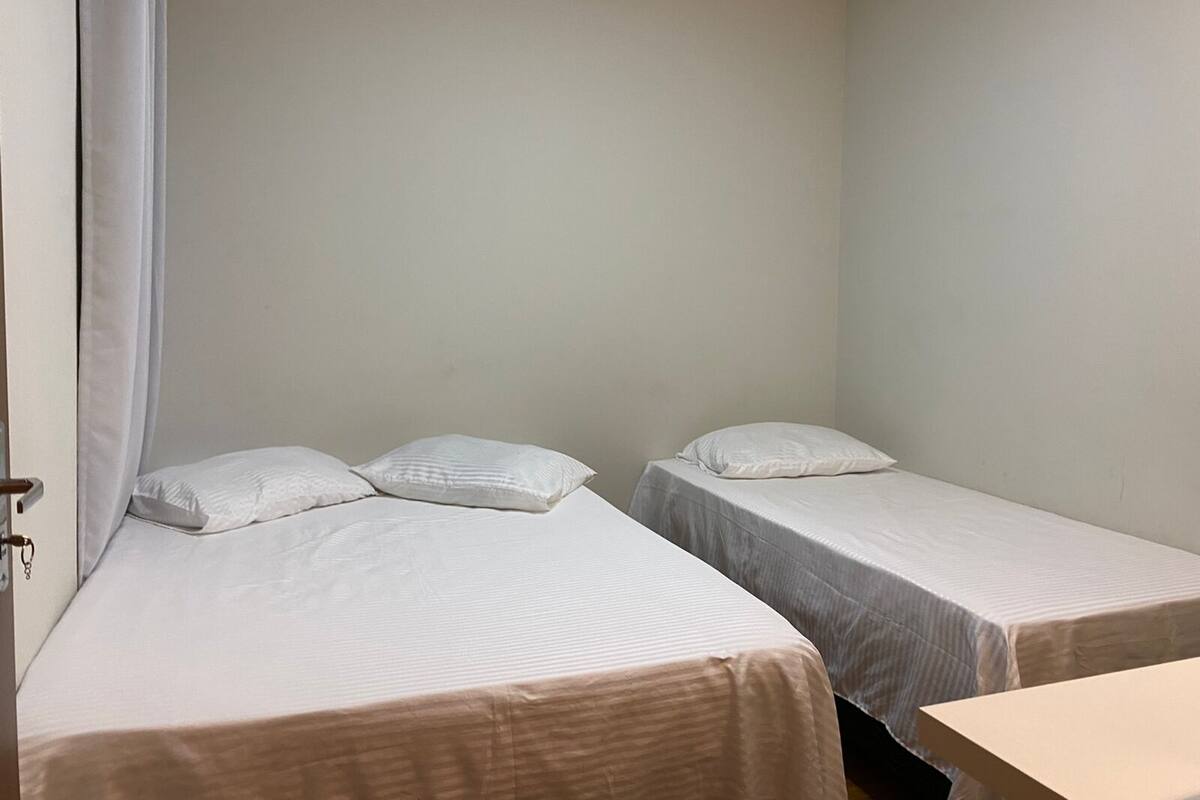 Um quarto pequeno e simples com duas camas de solteiro, cada uma com travesseiro e cobertura lisa.