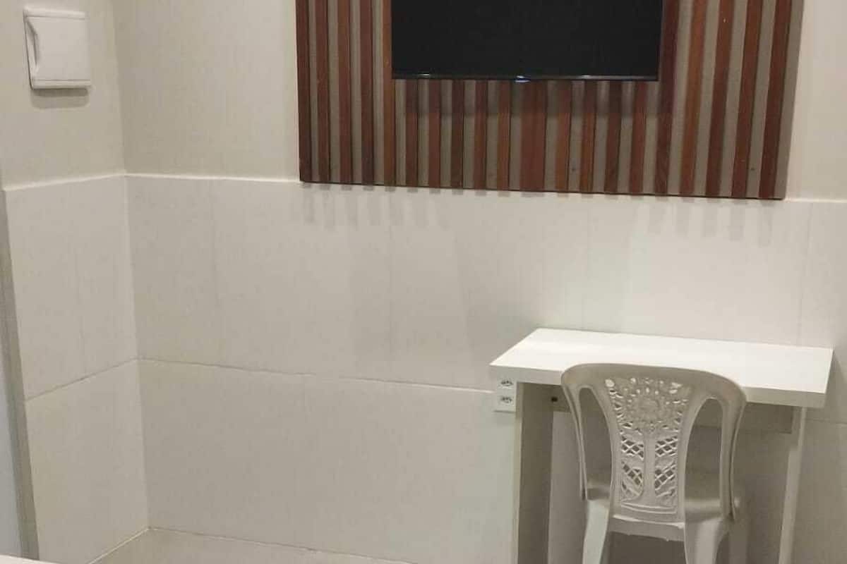 Quarto de hotel com cama, escrivaninha, cadeira e TV fixada em painel listrado.