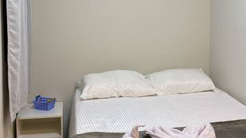Un dormitorio con una cama, almohadas, una mesita de noche y una cesta azul.