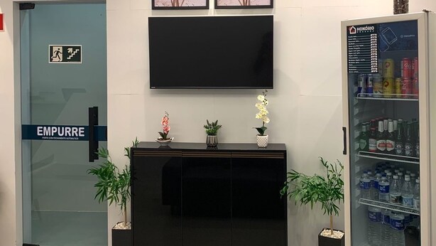 A reception area with a black console, a mounted TV, framed floral artwork, a refrigerator stocked with beverages, and a door labeled "EMPURRE". - Honório Pousada  (Tucano)