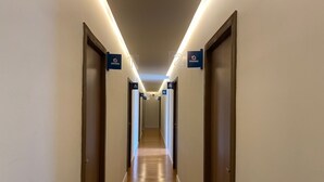 A hotel corridor with wooden floors, doors on both sides, and illuminated signs indicating room numbers. - Honório Pousada  (Tucano)