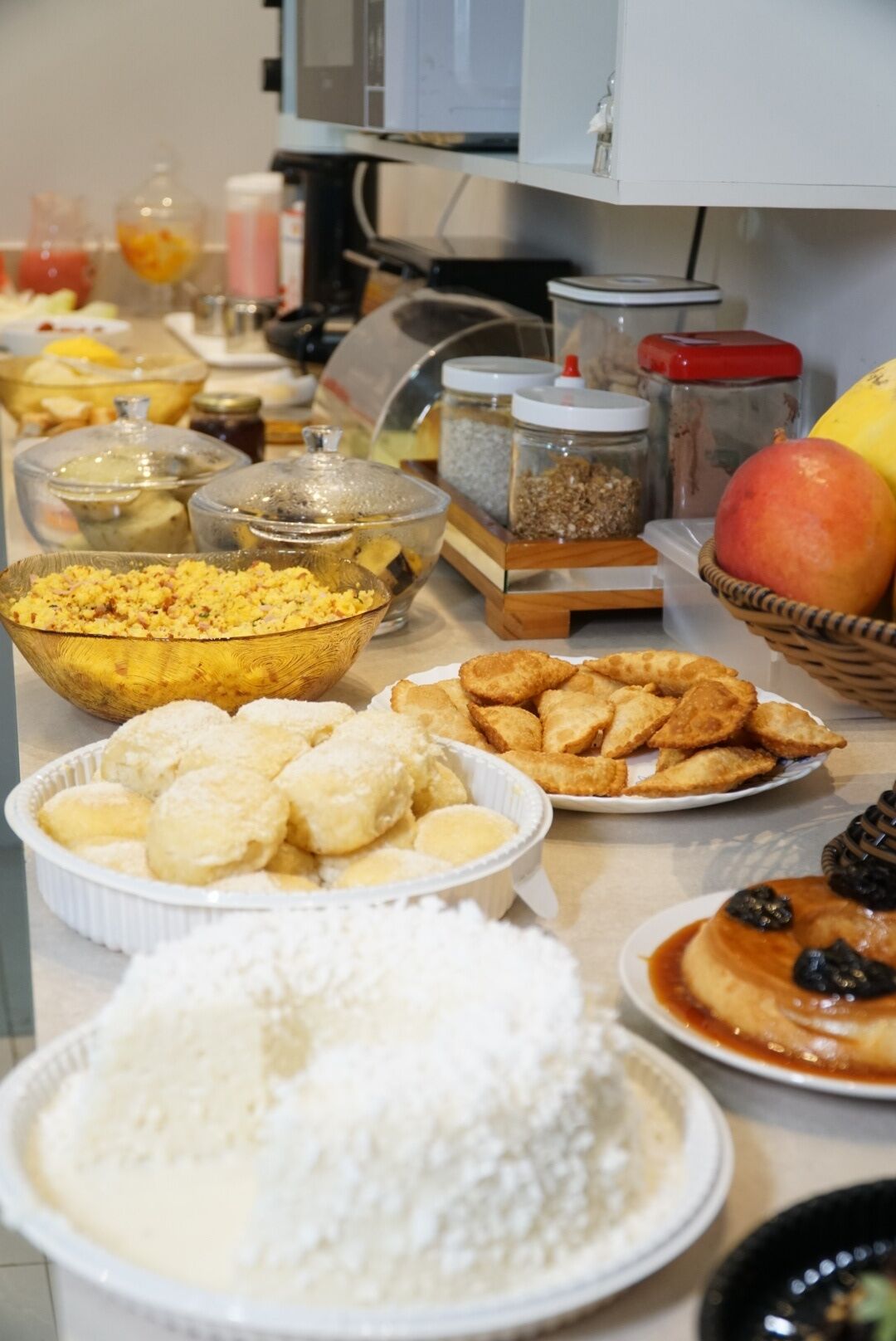 A buffet table with various food items including a bowl of rice, a plate of fried snacks, and a basket of fruits.