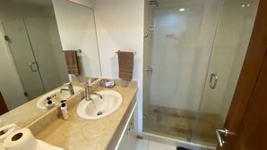 A bathroom with a double sink, a mirror, a glass shower enclosure, and a towel rack. - Departamentos QM1 (Mazatlán)