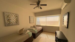 A bedroom with two beds, a ceiling fan, a window, and a desk. - Departamentos QM1 (Mazatlán)
