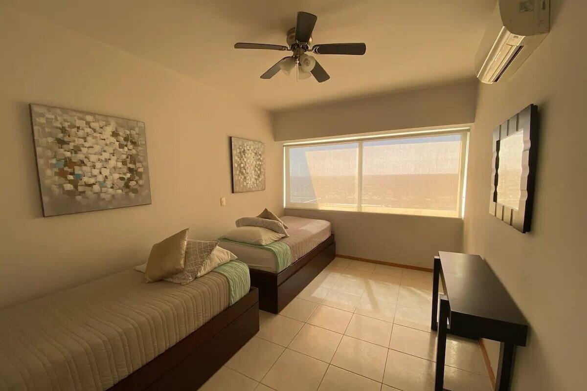 Un dormitorio con dos camas, ventilador de techo, ventana y escritorio.