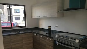 Una cocina con armarios de madera, una estufa y un ventanal con vistas a edificios y un coche rojo afuera.