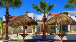 Un resort con sombrillas de paja, palmeras y edificios blancos modernos.