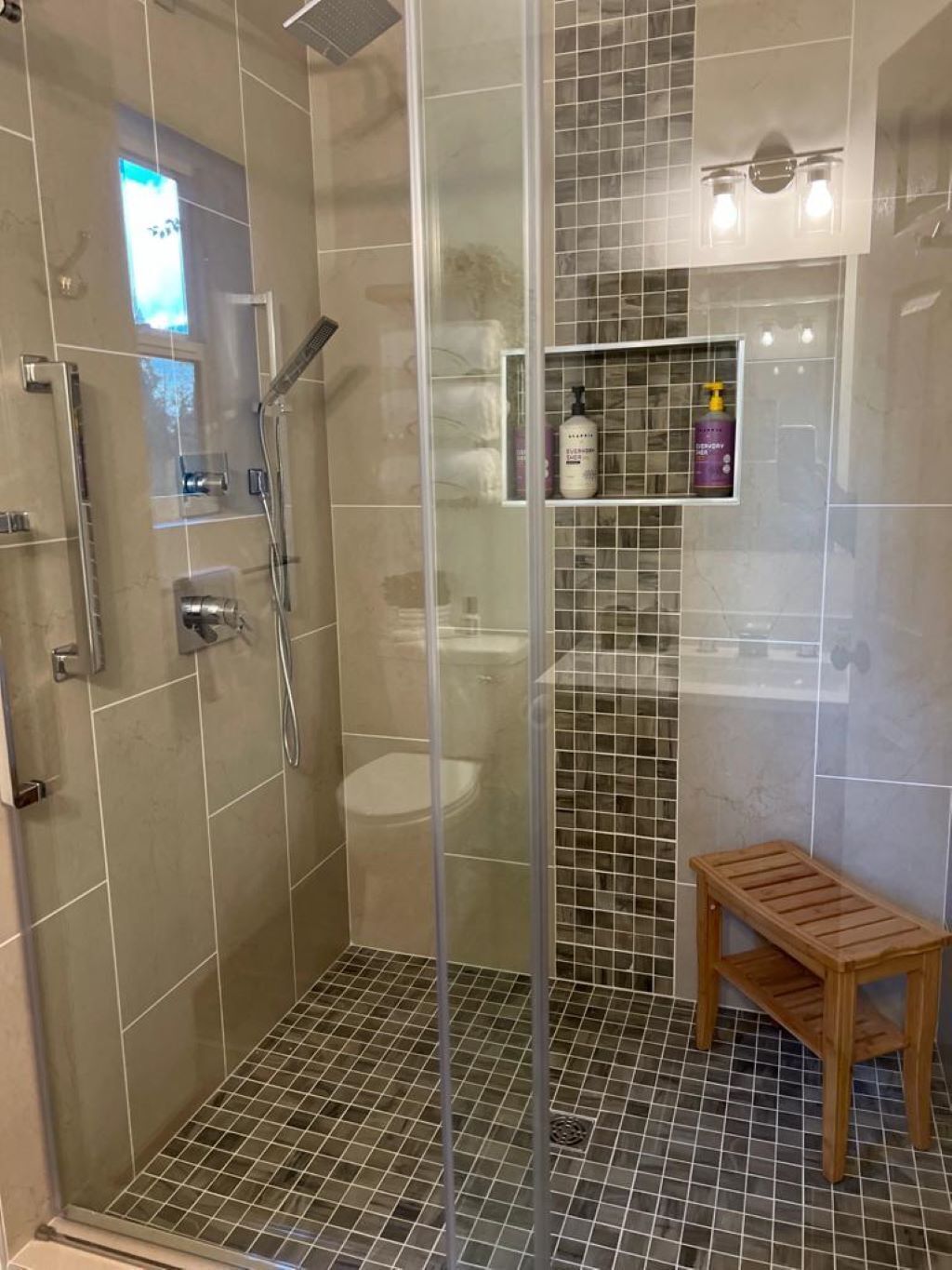 A shower area with a glass door, a wooden bench, and a tiled floor.