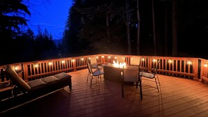Une terrasse extérieure dotée d’un foyer, de sièges et de guirlandes lumineuses.