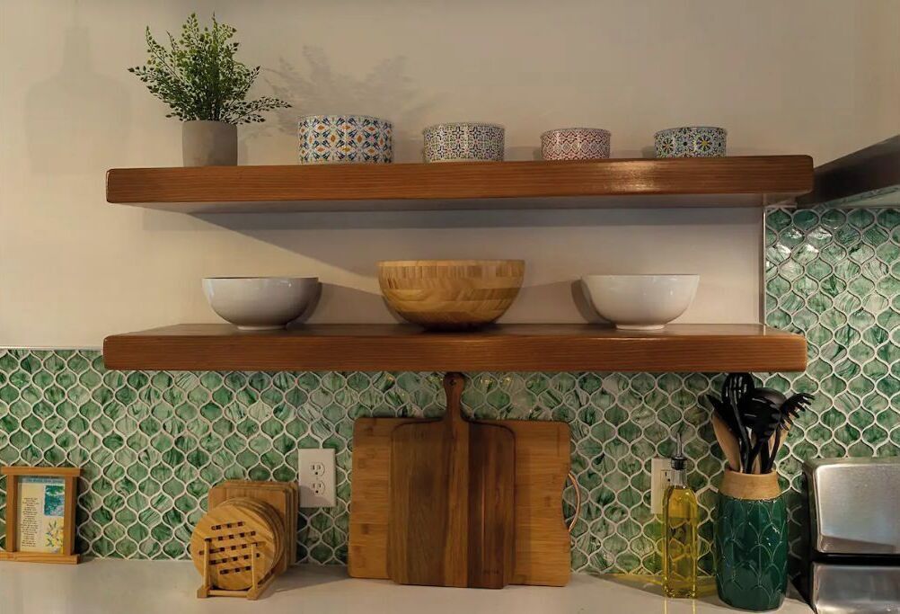 Een keuken met twee houten planken, een groene mozaïek achterwand en diverse keukengerei.