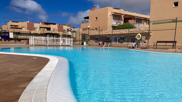 Ein Pool mit weißem Rand, umgeben von Gebäuden mit Balkonen und wolkenlosem Himmel.