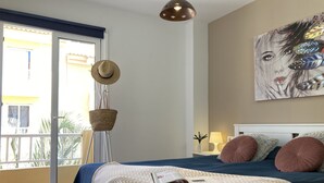 Ein Schlafzimmer mit Bett, Nachttisch mit Lampe, Wandbild und Balkon mit Blick.
