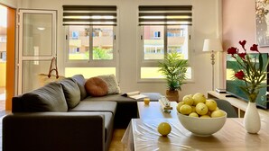 Ein modernes Wohnzimmer mit einer Couch, einem Esstisch mit einer Zitronenschale, einer Topfpflanze und einem Fernseher.