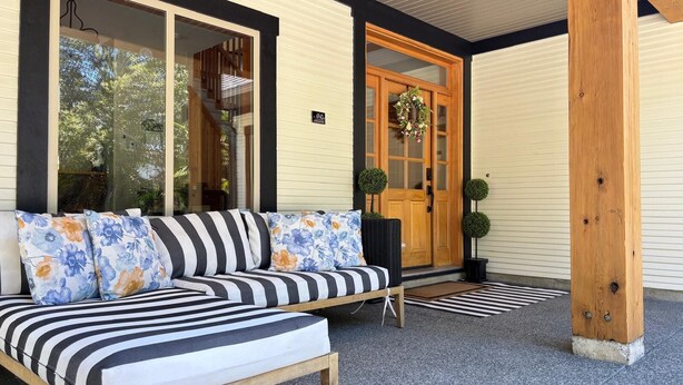 A modern outdoor seating area with a striped sofa, a wooden door with a flower wreath, and a small potted plant. - Seabrook Farmhouse with Hot Tub & Swimming Pool, 4 min to Butchart Gardens  (Saanichton)