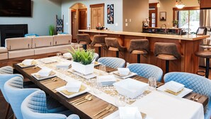 A dining area with a long table set for six, surrounded by blue upholstered chairs. - Seabrook Farmhouse with Hot Tub & Swimming Pool, 4 min to Butchart Gardens  (Saanichton)