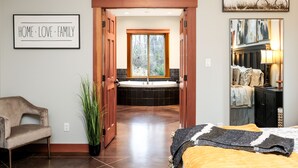 A bedroom with a bed, a chair, a potted plant, a framed picture, and a view of a bathroom with a bathtub. - Seabrook Farmhouse with Hot Tub & Swimming Pool, 4 min to Butchart Gardens  (Saanichton)