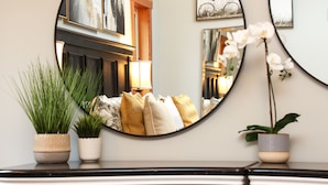 A mirror reflecting a room with a bed, pillows, a lamp, and two potted plants. - Seabrook Farmhouse with Hot Tub & Swimming Pool, 4 min to Butchart Gardens  (Saanichton)