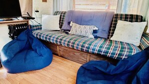 En mysig inredning i husbilen med en bäddsoffa, två sittpuffar, en tv och ett fönster med gardiner.