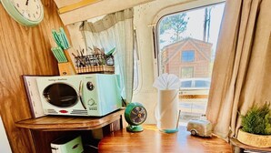Ett kompakt kök med ett träbord och turkosa barstolar, en gammal radio och ett fönster med utsikt över ett hus.