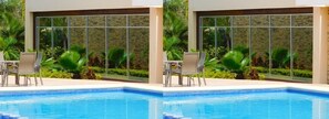 A swimming pool with two chairs and a table, surrounded by lush greenery and a stone wall.