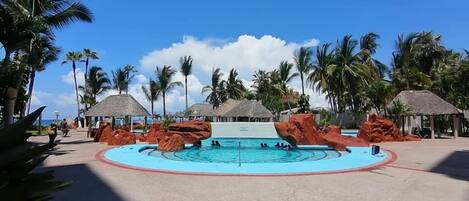 A pool area with palm trees and thatched-roof structures.