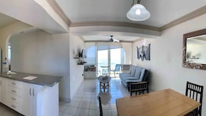 A spacious living area with a kitchen, dining table, and a balcony with a view. - Departamentos QM2 (Mazatlán)