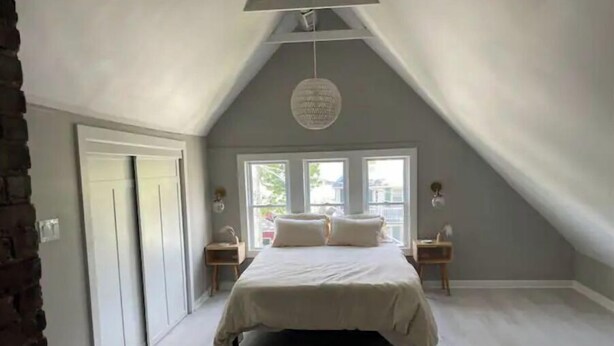 A bedroom with a sloped ceiling, a bed centered in the room, two bedside tables, and a window with a view of the outside. - Modern Large Studio Apartment in Heart of Tremont. (Cleveland)
