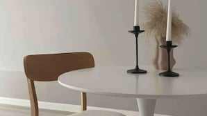 A round dining table with two tall white candles on black stands, a wooden chair, and a vase with dried plants. - Modern Large Studio Apartment in Heart of Tremont. (Cleveland)