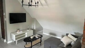 A modern living room with a grey sofa, a black coffee table, a white TV stand, and a black chandelier. - Modern Large Studio Apartment in Heart of Tremont. (Cleveland)