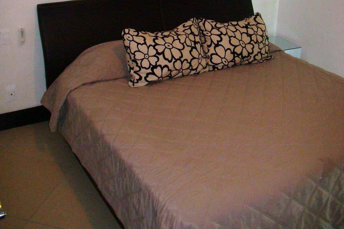 A bed with a dark headboard and a beige bedspread.