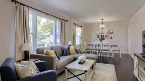 A living room with a sofa, coffee table, and dining area with chairs. - Cozy KC Suburb Home, Sleeps8_ PoolTable_ Foosbal (Mission)