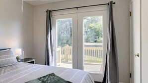 A bedroom with a bed, a nightstand, a lamp, and a view of a wooden deck through a sliding glass door. - Cozy KC Suburb Home, Sleeps8_ PoolTable_ Foosbal (Mission)