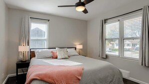A bedroom with a bed, nightstands, a ceiling fan, and windows with curtains. - Cozy KC Suburb Home, Sleeps8_ PoolTable_ Foosbal (Mission)